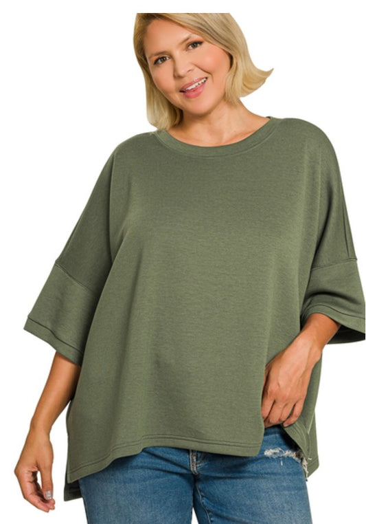 A woman wearing an olive green oversized short-sleeve top with a relaxed fit and blue jeans, photographed against a plain white background.