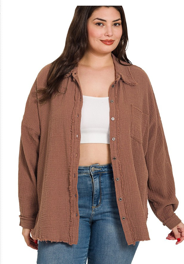 Woman wearing a brown button-up shirt over a white crop top and blue jeans on a white background