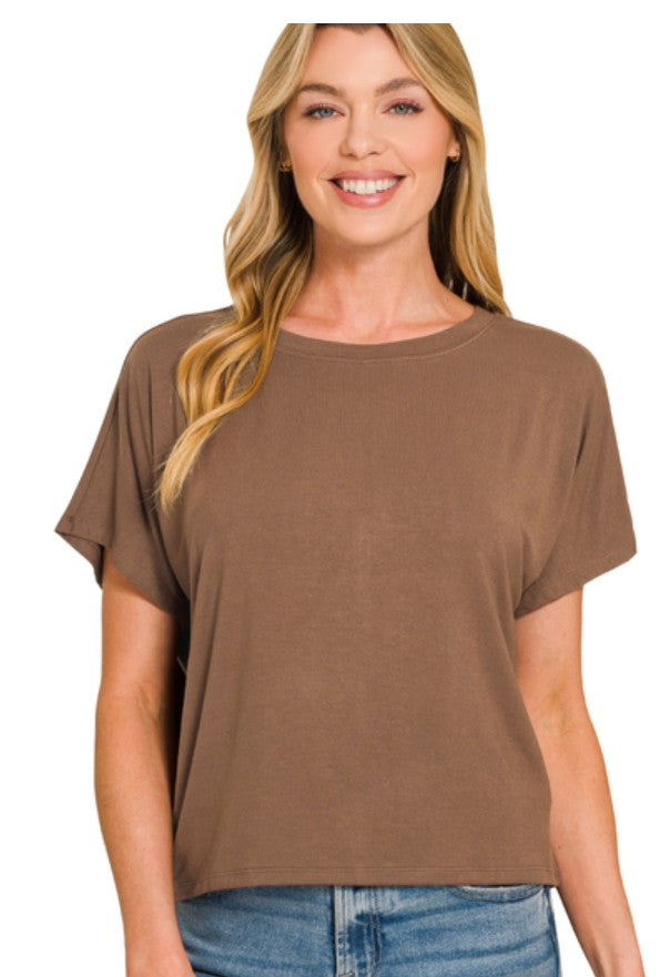 A smiling blonde woman wearing a brown short-sleeve crewneck top and blue jeans, photographed against a plain white background.