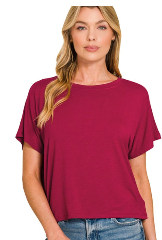 A woman wearing a short-sleeve crewneck top in a deep cabernet, paired with blue jeans, against a plain white background.