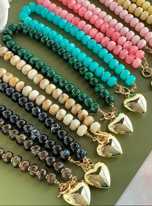 Chunky beaded necklaces with toggle claps and gold heart charms laying on a table 
