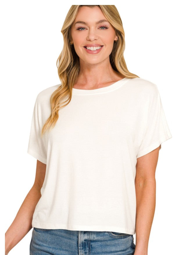 A woman wearing a cream-colored short-sleeve crewneck top and blue jeans, shown from the waist up against a plain white background.