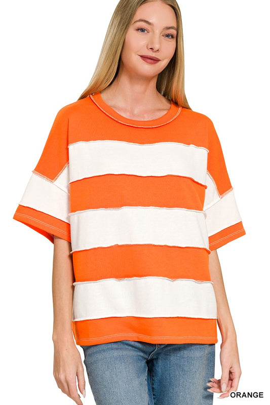 A woman wearing a short-sleeve crewneck top with bold horizontal orange and white stripes, paired with blue jeans, against a plain white background.