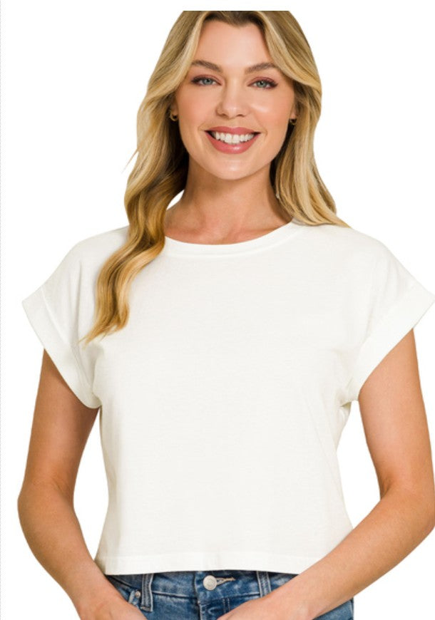 A smiling blonde woman wearing a short-sleeve crewneck crop top in off-white, paired with blue jeans, against a plain white background.