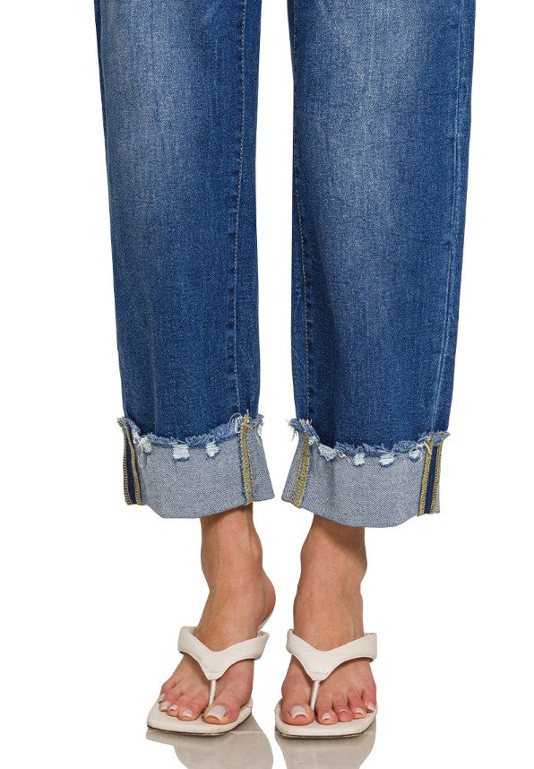 Blue jeans with rolled-up cuffs worn by a person on a white background